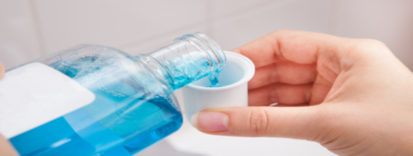Person pouring mouthwash with alcohol content into a rinse cup