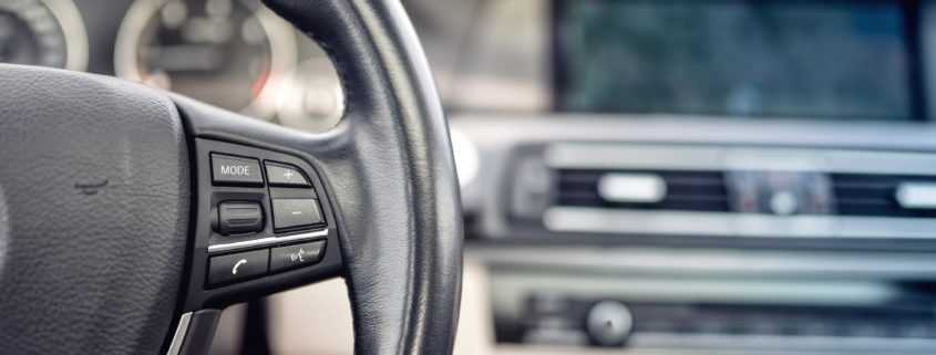 Vehicle steering wheel with details of buttons and adjustment controls in background