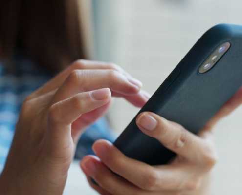 Woman in a blue shirt, scrolling on her phone.