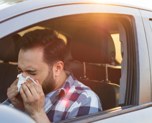 Man sneezing into a tissue in his car.