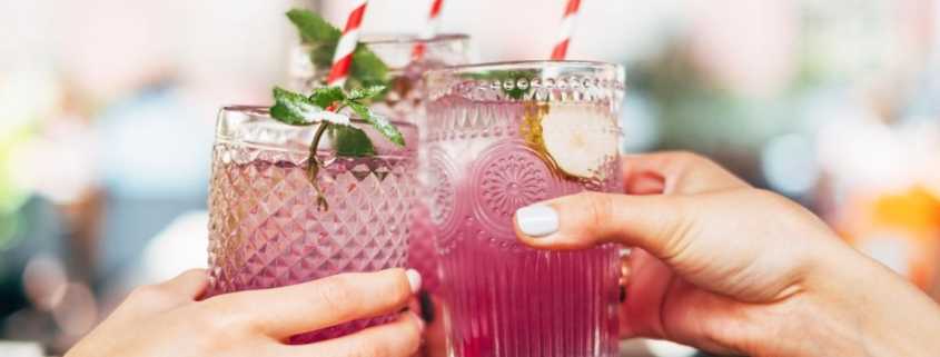 Hands toasting a pink alcoholic beverage in clear, decorative glasses for the blog Can I still drink alcohol with an Ignition Interlock Device