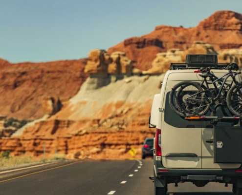 Sprinter van with bike rack driving on road with red rock in background
