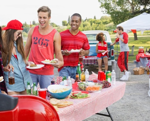 Friends,Eating,At,Tailgate,Barbecue,In,Field